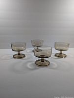 Four vintage smoky glass champagne cups arranged in a cluster on a flat surface, showing their shape and color.