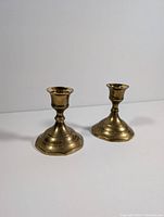 Pair of solid brass candlestick holders shown together on white background with slight shadows, highlighting the tiered octagonal bases and spindle stems.