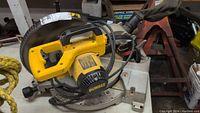 Side view of DeWalt compound miter saw showing yellow motor housing, power cord and metal base with angle markings.