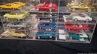 Front and side view of twelve die-cast collectible cars in clear display case showing multiple colors and styles.