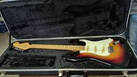 Full view of sunburst electric guitar inside open black plush-lined case