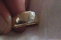 Front view of ring held between fingers showing white gold diagonal inlay with three diamonds.