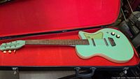 Full-length view of surf green Danelectro guitar inside hard case