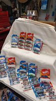 Several Hot Wheels cars new in packaging laid out on white fabric background, showing multiple blister packs each containing single die-cast car.