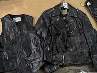 Black leather vest, biker jacket, and gloves laid on a flat surface