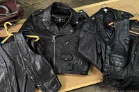 Photo showing two black leather jackets, parts of pants and vests are visible