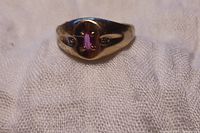 Front view of a men's gold ring with a pink oval center stone and small diamond chips on sides.