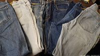Six pairs of men's jeans in various denim washes, visible belt loops and pockets indicating classic style casual jeans.