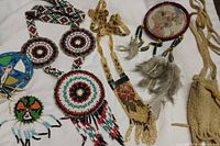 Overview of multiple Native American jewelry items including beaded medallions, feathered wall hanging, leather pouch.
