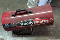 Top view of red cylindrical metal propane heater showing brand lettering and black handle on top