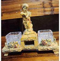 Front view of the antique Italian inkwell with cherub figurine, two glass inkwell holders, and floral decoration on base.