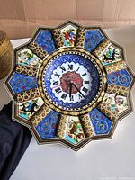 Front view of the octagonal wall clock showing detailed painted porcelain panels with horseman and animal scenes alternating with blue and gold floral swirl patterns surrounding the clock face with Roman numerals.