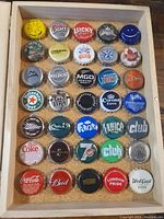 Top-down photo showing all 35 bottle caps arranged in rows in the wooden display box.
