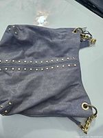 Michael Kors Astor leather shoulder bag laying flat showing gold-tone studs and side details.