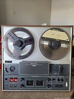 Front view with supply and take-up reels loaded, showing control panel, VU meters and tape speed selector