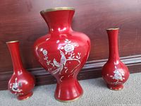 Three vintage brass vases with red enamel and mother of pearl cloisonne decorations, displayed on floor against wood background