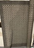 Photo showing a grey and off-white geometric patterned area rug with a darker grey diamond border.