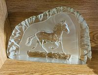 Clear glass horse figurine measuring about 5-6 inches wide, showing the horse in mid-trot, set on a flat base with textured edge and smooth interior.