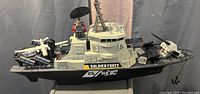 Large toy military boat labeled Soldier Force with mounted weapons and small airplane and helicopter on deck.