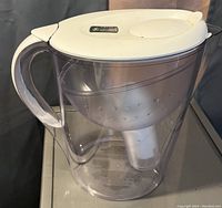 Clear plastic Brita water filter jug with white lid and handle, showing internal filter compartment and digital indicator on lid.