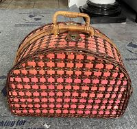 Closed view of the woven wicker picnic basket showing rounded top, handle, and metal latch with brown lattice pattern.