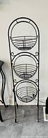 Front view of the three tier rod iron fruit stand showing all three baskets mounted vertically on a metal frame.