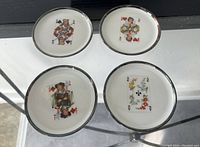 Four vintage butter patty plates shown from top with playing card character illustrations on white porcelain and silver overlay rims.