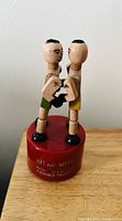Full view of two wooden boxer figurines standing on a red round base, facing each other in a boxing stance.