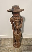 Front view of large vintage wooden floor figurine showing a carved man wearing a broad hat using a pestle and mortar