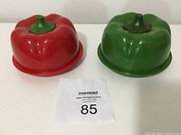Red and green bell pepper-shaped pepper keepers displayed side by side, showing their shape and colors.