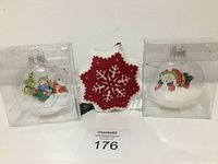 Photo showing three new Christmas ornaments: two clear plastic snowglobes with festive figurines inside and one red fabric snowflake ornament.