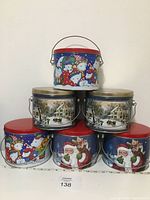 Full view of six round Christmas tins arranged in two rows. Top row includes two tins with winter home scene and one small tin with snowman design on top. Bottom row includes a snowman tin and two Santa Claus tins.