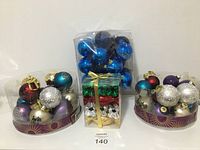 Wide view of all ornaments including sets of colored balls in plastic trays, blue balls in a plastic box, and candy-shaped ornaments in a clear box with gold ribbon.