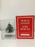 Photo of miniature musical Christmas tree inside clear plastic case, shown next to original red box labeled Musical Fantasy.
