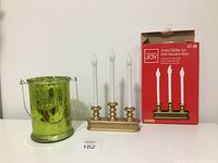 Green glass candle holder and battery operated candle set displayed side by side, showing candle holder's reflective finish and candle set's gold wooden base and white candles.