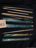 Top-down view showing multiple metal knitting needles of various lengths including sets in plastic sleeves along with loose needles.