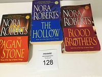 Photo of three Nora Roberts paperback books: The Pagan Stone, The Hollow, Blood Brothers, all part of the Sign of Seven Trilogy series, placed on a white surface.