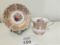Paragon teacup and saucer facing front showing gold ornate design with floral artwork in center