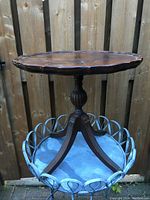 Front view of vintage wooden pie crust table with brass feet against wooden fence background.