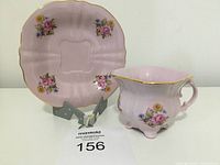 Front view of pink square teacup and saucer with floral designs and gold trim