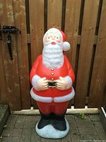 Front view of the 40-inch tall Santa Claus blow mold decorated in a red suit with white trim, black boots, and a gold buckle belt against a wooden fence background.