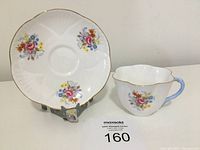 Front view of Shelley fine bone china teacup and saucer with floral design and blue handle on teacup