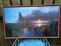 Framed landscape print showing Cotopaxi volcano scene with dramatic sky and natural features, behind glass and bamboo style frame.