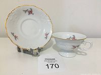 Cup and saucer displayed on a stand showing front design and gold rim detail.