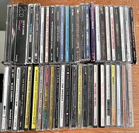 Photo showing a horizontal stack of 45 jewel case music CDs with visible spines showing artists and album names such as Pink Floyd, Eminem, Van Halen, and others.