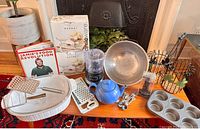 Photo showing all items on table including casserole dish with lid, boxed Sorbet dessert dishes, graters, teapot, mini electric chopper, screw pulls, muffin pan, cookbooks, colander, and small basket.