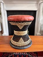 Side view of woven black and natural rattan wicker drum-shaped stool with leather seat and decorative weaving pattern.