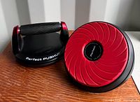 Two Perfect Fitness rotating pushup handles with black grips and red swivel bases, shown on wooden surface.