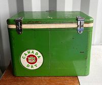 Front view showing green cooler with Canada Dry circular logo and metal latches.