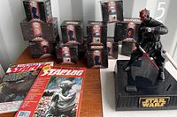 Photo of the Darth Maul figure with 12 boxed Star Wars collectible toys and two Starlog magazines on a table.